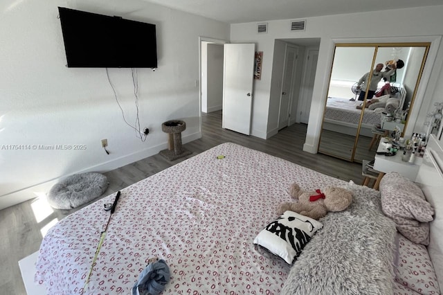 bedroom with multiple closets, baseboards, visible vents, and wood finished floors