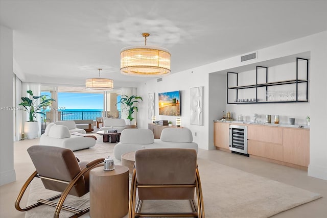 living area with concrete flooring, a notable chandelier, beverage cooler, visible vents, and indoor wet bar