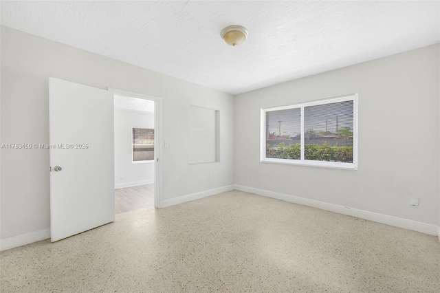 unfurnished room featuring a wealth of natural light, a textured ceiling, and baseboards