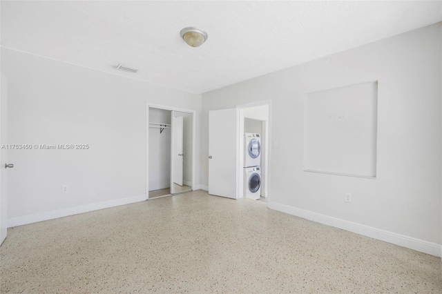 unfurnished room featuring a textured ceiling, stacked washer and dryer, visible vents, and baseboards