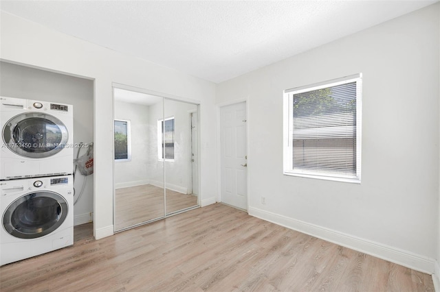 laundry area featuring a wealth of natural light, stacked washer / dryer, laundry area, and light wood finished floors