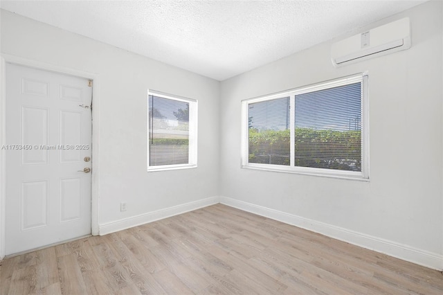 unfurnished room with light wood-style floors, an AC wall unit, a textured ceiling, and baseboards