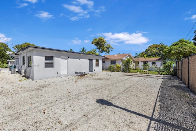 rear view of house with central air condition unit, fence, and stucco siding