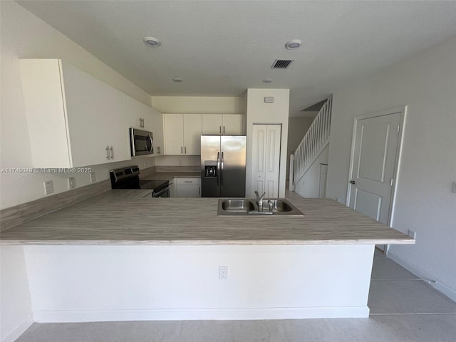 kitchen featuring visible vents, a peninsula, stainless steel appliances, light countertops, and a sink