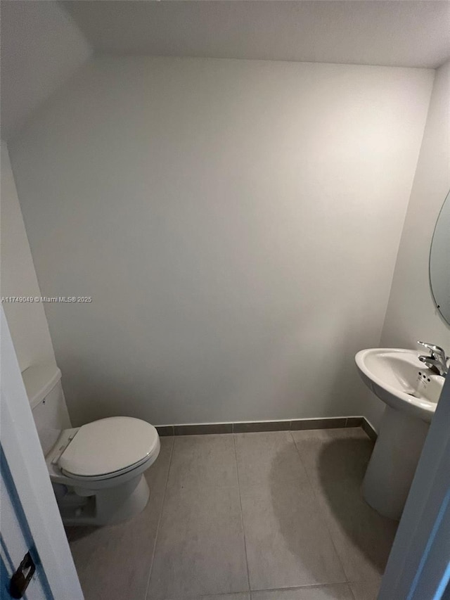 half bathroom featuring a sink, tile patterned flooring, toilet, and baseboards