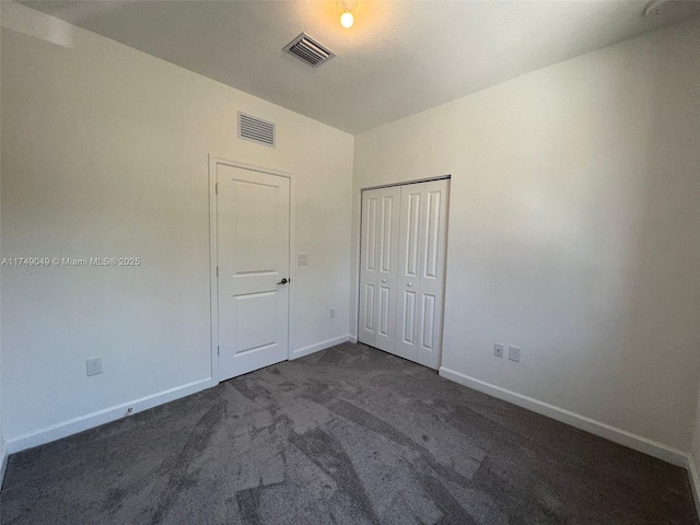 unfurnished bedroom featuring dark colored carpet, a closet, visible vents, and baseboards