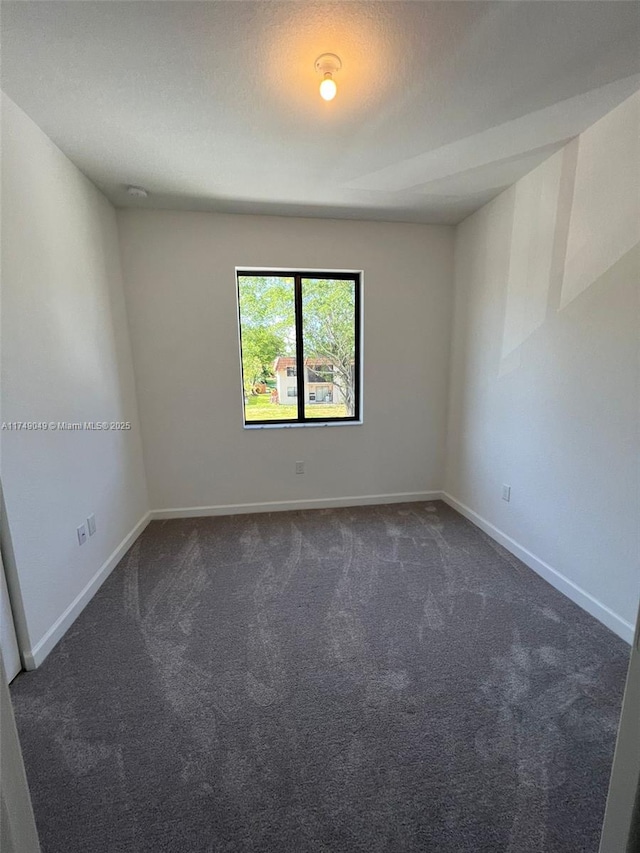 spare room with dark carpet and baseboards