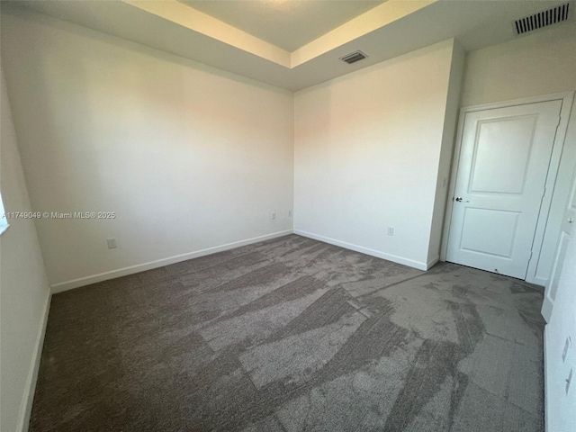 carpeted empty room featuring baseboards, visible vents, and a tray ceiling