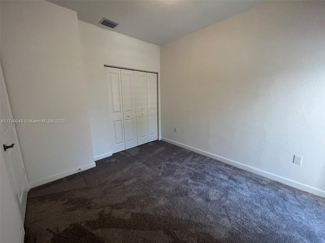 unfurnished bedroom with baseboards, visible vents, dark carpet, and a closet