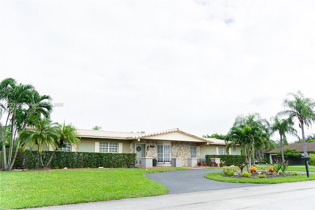 single story home with a front yard, a tile roof, driveway, and stucco siding