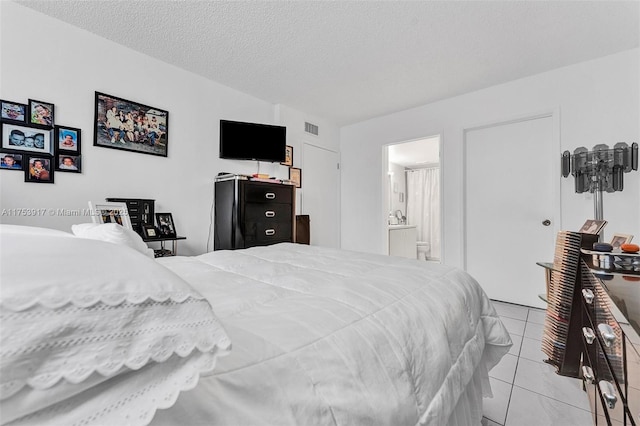 bedroom with connected bathroom, visible vents, a textured ceiling, and tile patterned floors