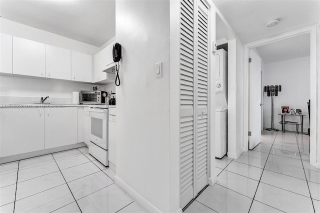 kitchen featuring a sink, stacked washer / drying machine, white cabinets, light countertops, and electric stove