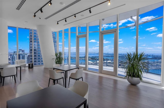 dining space featuring a city view, a water view, wood finished floors, visible vents, and a wall of windows