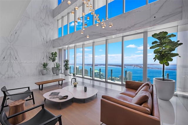 living area featuring a water view, a high ceiling, floor to ceiling windows, and wood finished floors