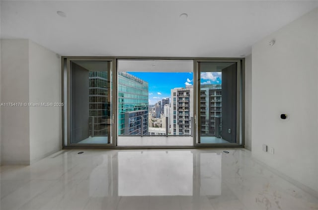 unfurnished room featuring expansive windows, marble finish floor, a city view, and baseboards