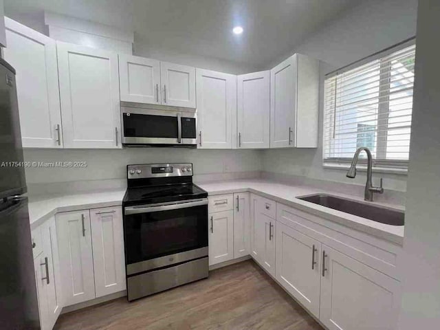 kitchen with a sink, stainless steel appliances, light countertops, white cabinets, and light wood-style floors