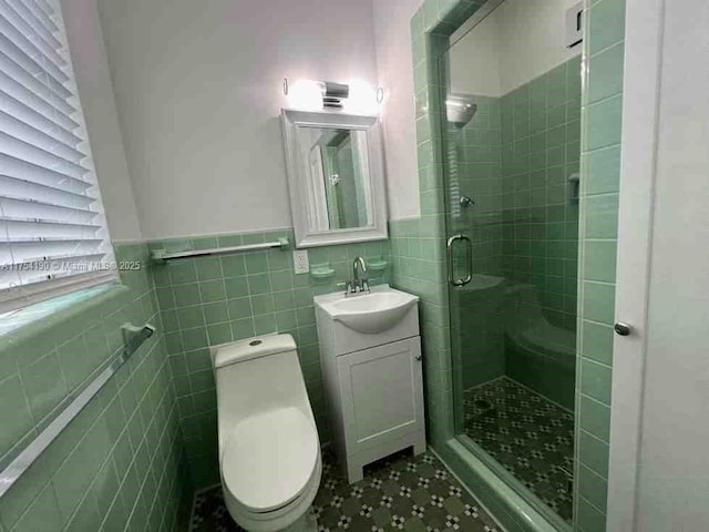 bathroom with a shower stall, a wainscoted wall, toilet, vanity, and tile walls