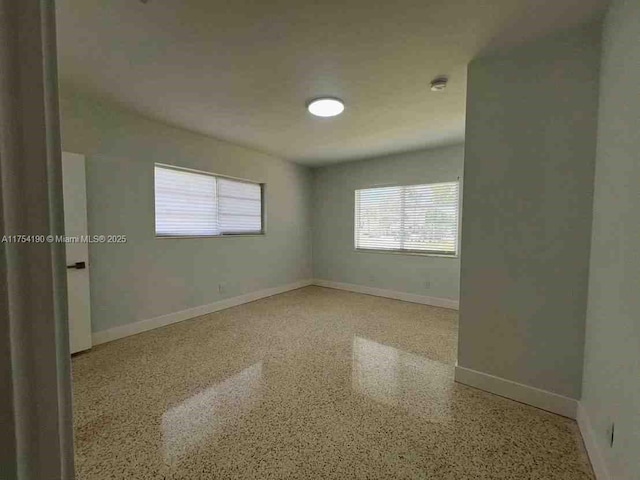 spare room with baseboards, speckled floor, and a wealth of natural light