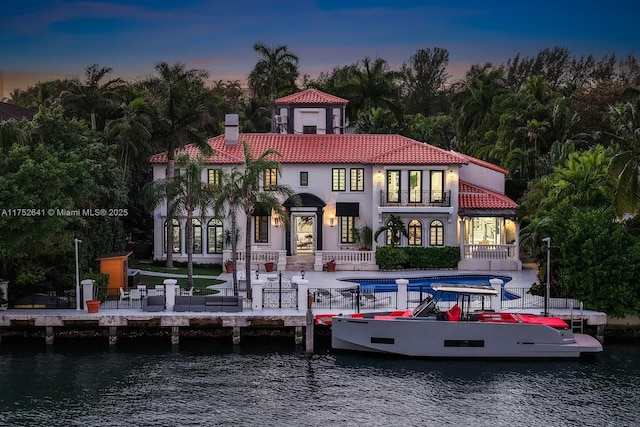 back of house at dusk featuring a patio area, a balcony, and a water view