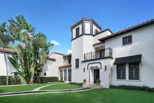 view of front of property featuring a front yard, a tiled roof, a balcony, and stucco siding