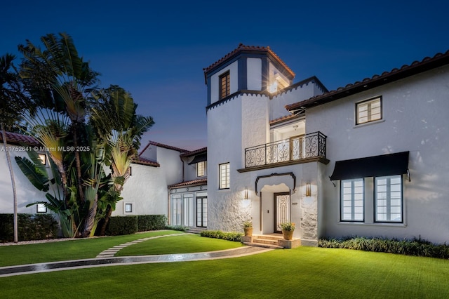 mediterranean / spanish-style house featuring a tiled roof, a front lawn, a balcony, and stucco siding