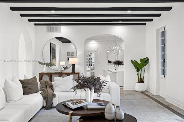 living room featuring arched walkways, visible vents, beamed ceiling, and baseboards