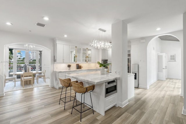 kitchen with tasteful backsplash, visible vents, arched walkways, light wood-type flooring, and a chandelier