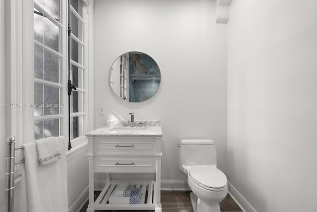 half bathroom featuring wood finished floors, vanity, toilet, and baseboards