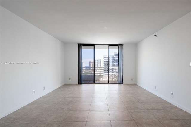 spare room featuring floor to ceiling windows, a city view, baseboards, and light tile patterned flooring