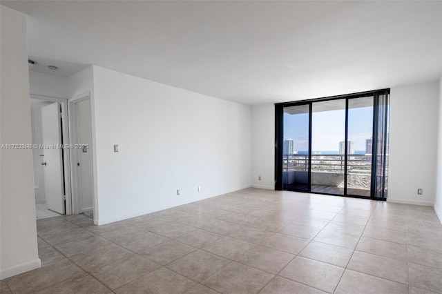 spare room featuring a view of city, floor to ceiling windows, baseboards, and light tile patterned floors