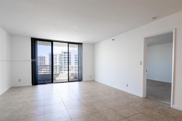 spare room with expansive windows, a city view, baseboards, and light tile patterned floors