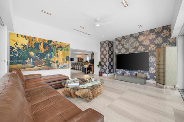 living area with an accent wall, ceiling fan, baseboards, and wallpapered walls