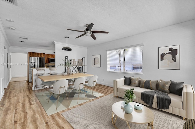 living area featuring a textured ceiling, light wood-type flooring, visible vents, and crown molding