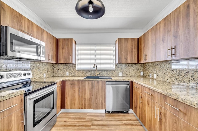 kitchen with light stone countertops, crown molding, appliances with stainless steel finishes, and a sink