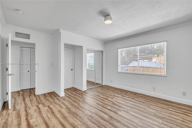 unfurnished bedroom with visible vents, crown molding, and light wood finished floors