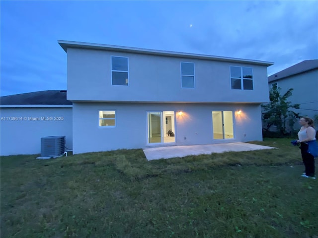 rear view of house featuring stucco siding, a lawn, central AC, and a patio