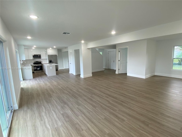 unfurnished living room featuring light wood-style flooring, recessed lighting, a sink, visible vents, and baseboards