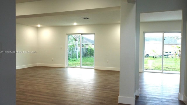 empty room with dark wood-style flooring, plenty of natural light, and visible vents