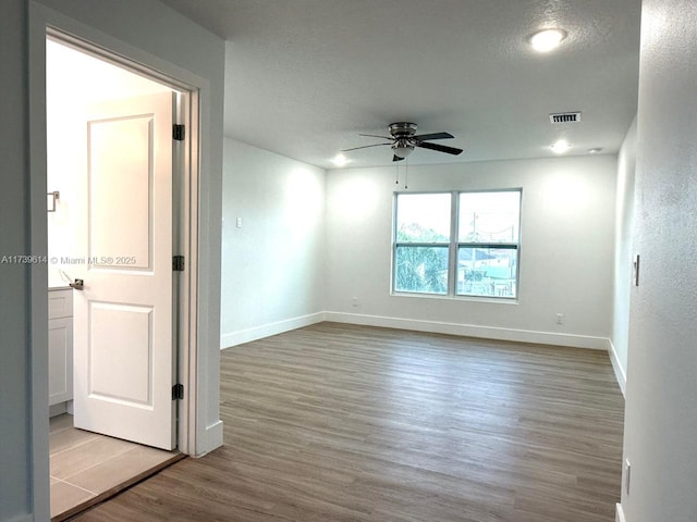 spare room featuring baseboards, visible vents, a ceiling fan, wood finished floors, and a textured ceiling