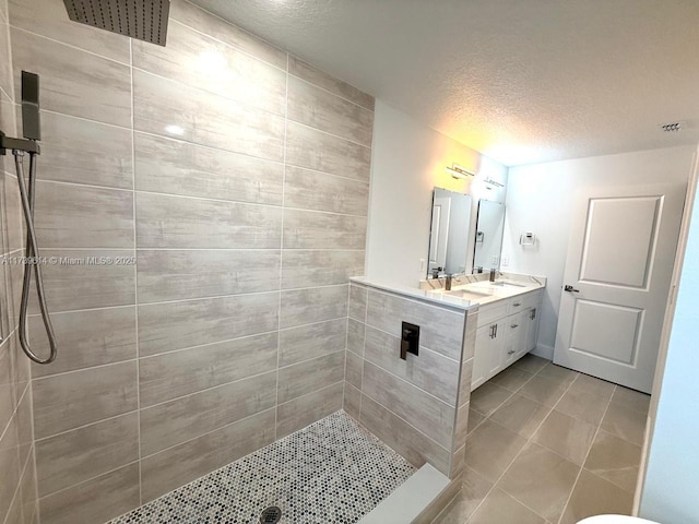 full bath featuring double vanity, a tile shower, a textured ceiling, a sink, and tile patterned floors