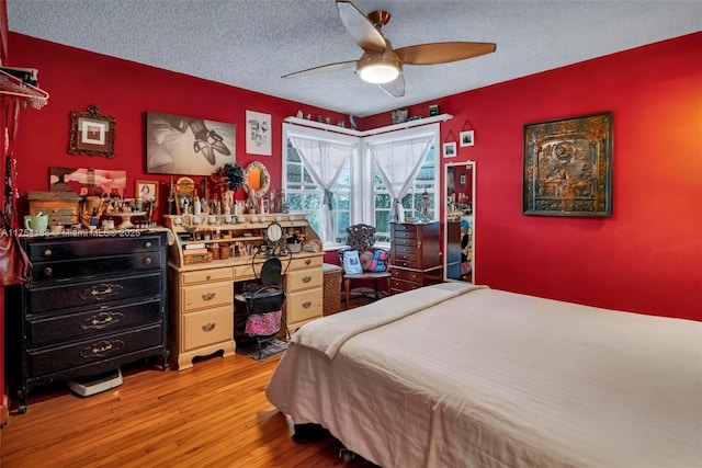 bedroom featuring a textured ceiling, ceiling fan, light wood-type flooring, and an accent wall