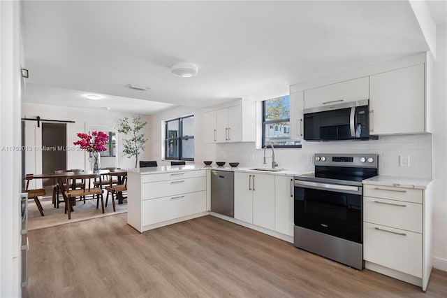 kitchen featuring stainless steel appliances, a peninsula, a sink, white cabinets, and light countertops