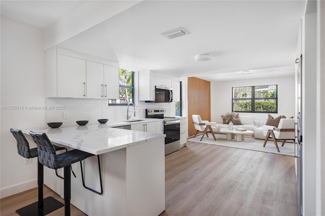 kitchen with stainless steel appliances, visible vents, backsplash, a sink, and a peninsula