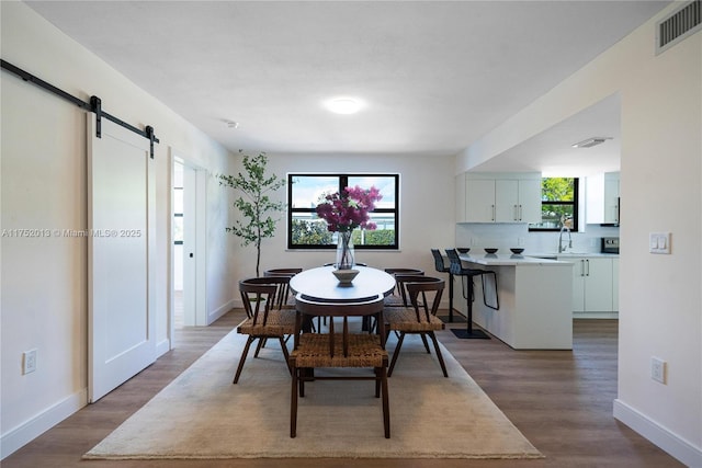 dining area with baseboards, a barn door, visible vents, and wood finished floors