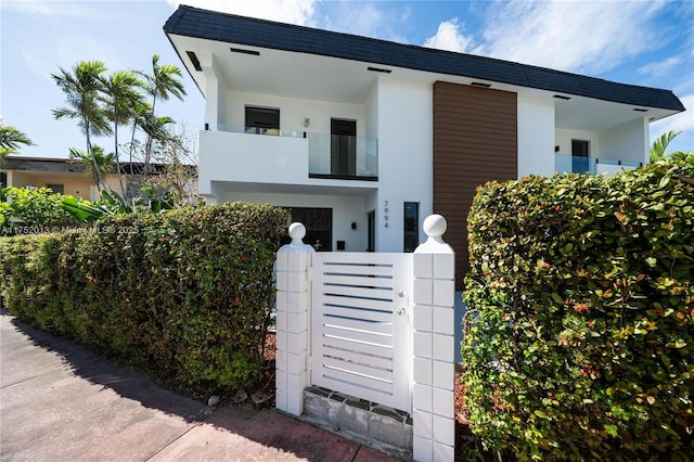 contemporary house featuring a balcony, a fenced front yard, a gate, and stucco siding