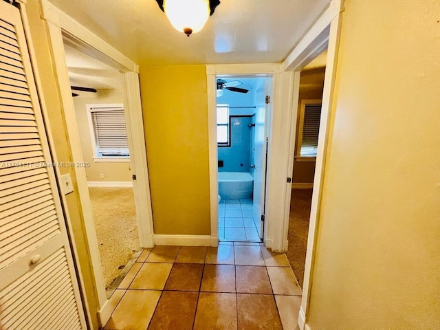 hallway with baseboards, carpet flooring, and tile patterned floors