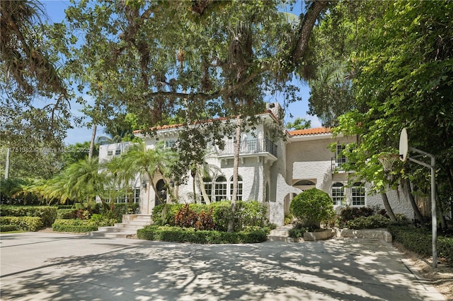 mediterranean / spanish home featuring a balcony, a tiled roof, and stucco siding