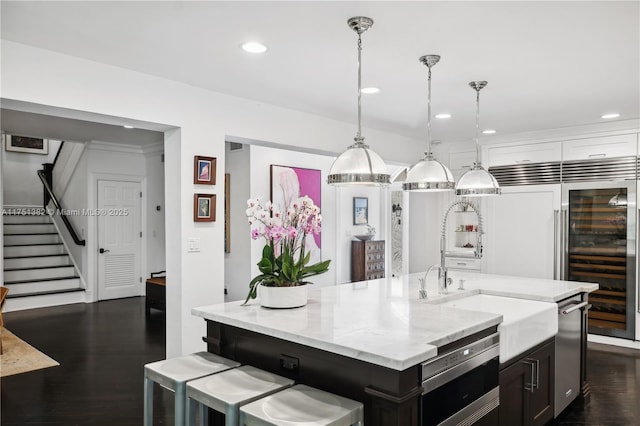 kitchen featuring dark wood-type flooring, pendant lighting, a kitchen island with sink, and light stone countertops