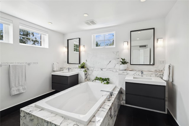 full bath featuring a bath, visible vents, two vanities, and a sink