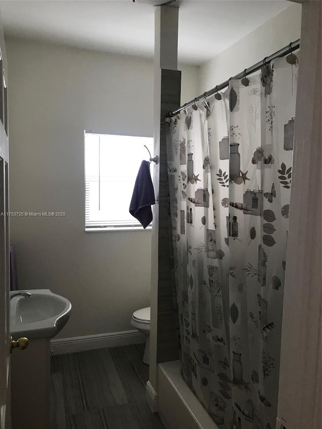 bathroom featuring shower / bath combination with curtain, toilet, baseboards, and a sink